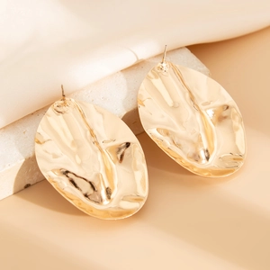 Detailed view of irregular oval gold earrings with hammered texture on silk fabric