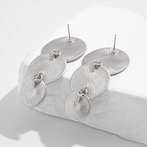 Detailed macro view of triple-layered round metal drop earrings with sunburst texture