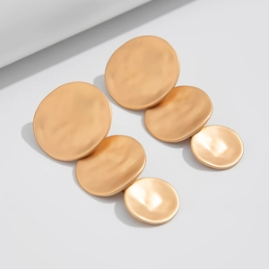 Close-up of triple matte gold drop earrings with tiered geometric circular disks