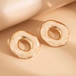 Dettaglio ravvicinato di orecchini dorati in metallo liquido su sfondo beige artistico