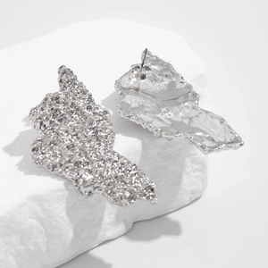 Macro detail of silver drop earrings with irregular lava texture on white stone