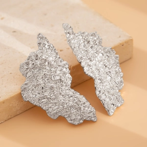 Detailed close-up of textured irregular silver droplet earrings on a stone display