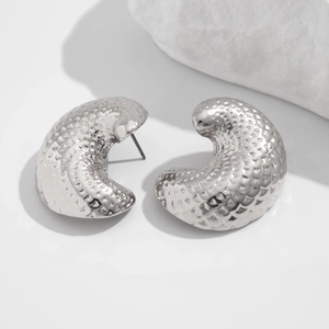 Macro detail of silver C-shaped earrings with hammered texture on white stone background