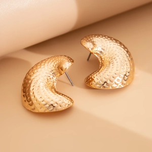 Macro shot of gold teardrop earrings with textured hammered finish on beige surface