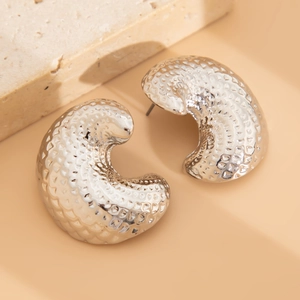 Macro shot of silver C-shaped chunky earrings with hammered texture and metallic luster