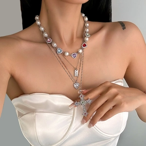 Detail van gelaagde ketting met kruishanger, parels en kleurrijke edelstenen