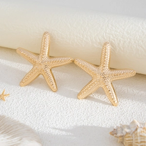 Detailed view of gold starfish earrings with realistic textured surface on sandy backdrop