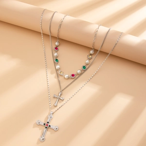 Detail van gelaagde zilveren ketting met kruishangers en parels bij zacht sfeerlicht