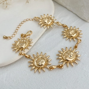 Détail de pendentifs soleil vintage dorés et fermoir homard sur une chaîne de cheville