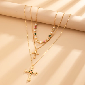 Detailopname van een drielaagse gouden ketting met kruis, parels en gekleurde stenen