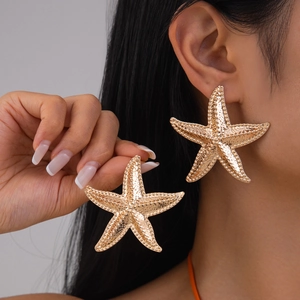 Close-up of oversized gold starfish stud earrings with realistic textured finish on model