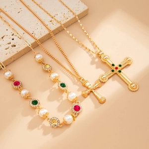 Detail van gouden kruis hanger ketting met parels en rode en groene edelstenen
