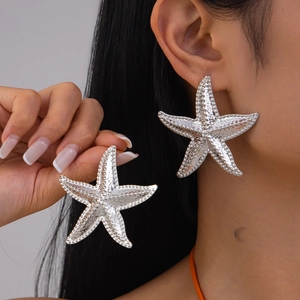 Close-up of oversized silver starfish earrings with textured 3D beaded finish on model