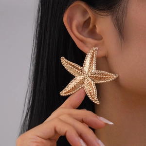 Close-up of oversized gold starfish earring with textured metallic finish on model
