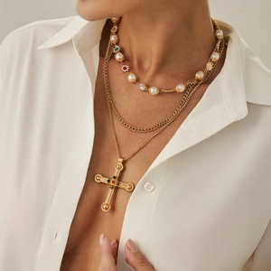 Detail van gelaagde gouden ketting met kruishanger, gekleurde edelstenen en parels