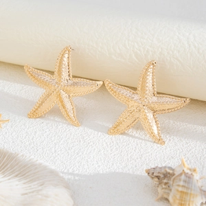 Macro detail of golden starfish earrings with textured surface on beach theme background