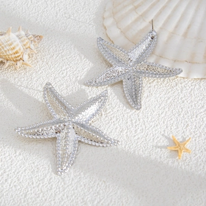 Detailed macro shot of silver starfish earrings with fine granular metallic texture