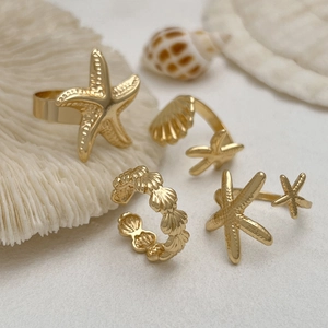 Detail shot of ocean theme gold rings with starfish and shell motifs on coral background