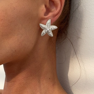 Detailed close-up of a silver starfish earring with white pearls on a model ear