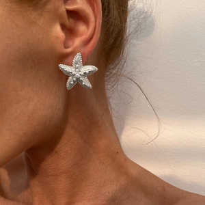 Detailed view of silver starfish earrings with pearls worn by a model in beach style