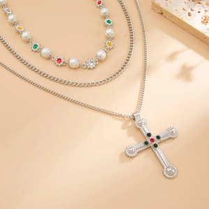 Detail van een drielaagse ketting met een vintage kruishanger en parel bloemenketting