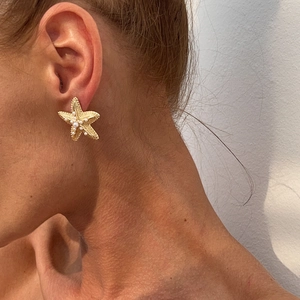 Detailed close-up of golden starfish earrings featuring faux texture and white pearls