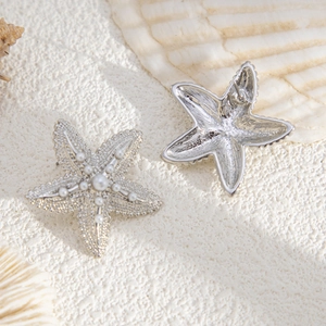 Macro detail of silver starfish earrings with white pearls on a beach sand background