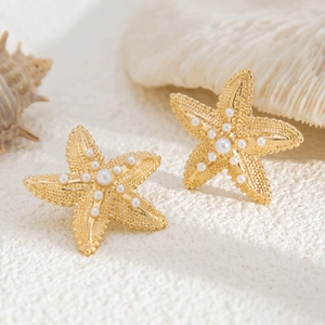 Detail of matte gold starfish earrings with white pearls on a beach-themed background