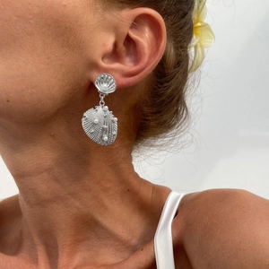 Close-up of silver shell earrings with white pearl accents on model for beach style