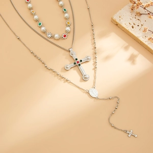 Detail van een gelaagde ketting met kruishanger, parels en kleurrijke edelstenen