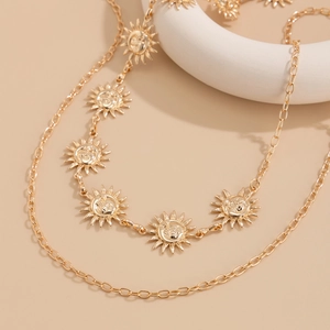 Détail de colliers dorés superposés avec pendentifs soleil et lune sur fond beige neutre