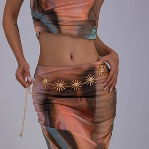 Détail d'une chaîne de taille dorée avec pendentifs soleil sur un ensemble tie-dye