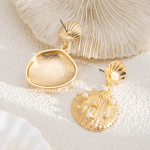 Detail of gold shell earrings featuring white pearls and metallic texture on a coral base