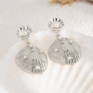 Macro detail of seashell-shaped silver earrings with pearl inlay on a beach prop
