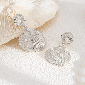 Detail of silver shell earrings with pearls on white coral, marine holiday style jewelry