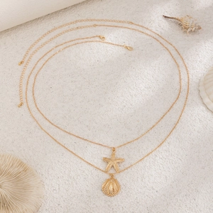 Detailed close-up of double-layer gold chain with starfish and shell pendants on sand
