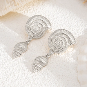 Macro detail of silver nautical shell earrings on a textured beach sand background