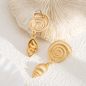 Detail view of gold nautilus and shell drop earrings on a white coral background