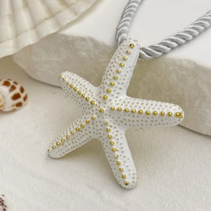 Detalle macro del colgante de estrella de mar de cerámica blanca con puntos dorados y cordón