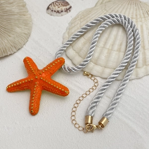 Detalle del collar de estrella de mar con colgante naranja y cuerda plateada en arena blanca