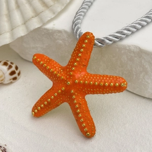 Detalle macro del colgante de estrella de mar naranja brillante con puntos dorados sobre piedra