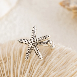 Macro detail of silver starfish earring with vintage texture on white coral background