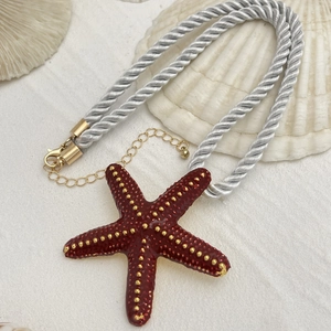 Detalle del colgante de estrella de mar roja con puntos dorados en cordón trenzado