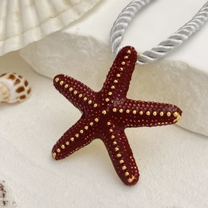 Collar colgante estrella de mar roja con puntos dorados sobre fondo de playa