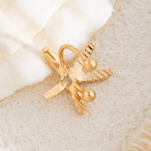 Detailed close-up of golden starfish ear cuff with textured surface on a white seashell