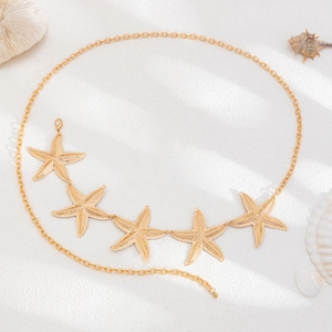 Detail of golden bohemian starfish body chain with textured pendants on beach sand