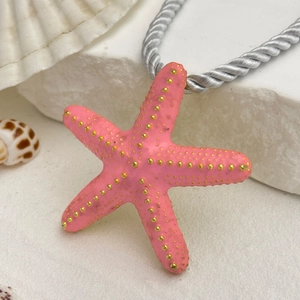 Detalle del collar con colgante de estrella de mar rosa y puntos dorados sobre piedra