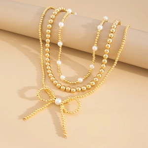 Detailed close-up of a three-layer gold bead and faux pearl necklace with bow pendant
