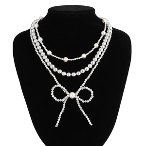 Macro detail of multi-layer faux pearl necklace with a beaded bow pendant on a neck display