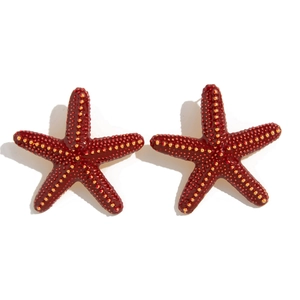 Detalle de pendientes de estrella de mar rojo oscuro con perlas doradas y acabado pulido